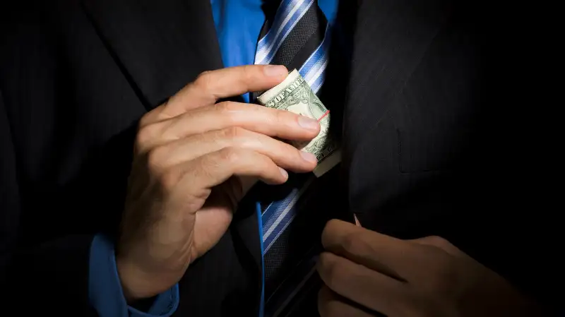 businessman putting wad of bills in suit