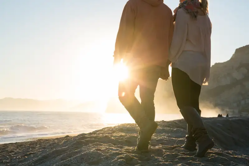 Couple walk hand in hand along beach, sunrise