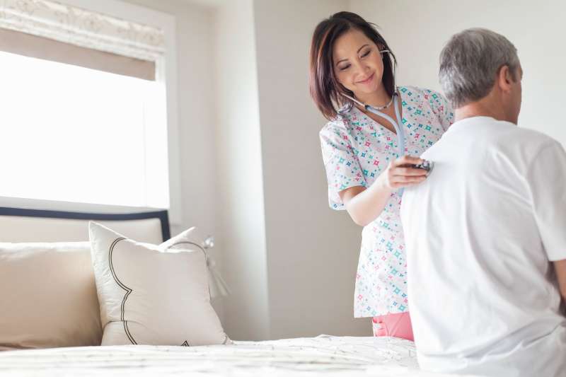 Female nurse examining senior man with stethoscope at home