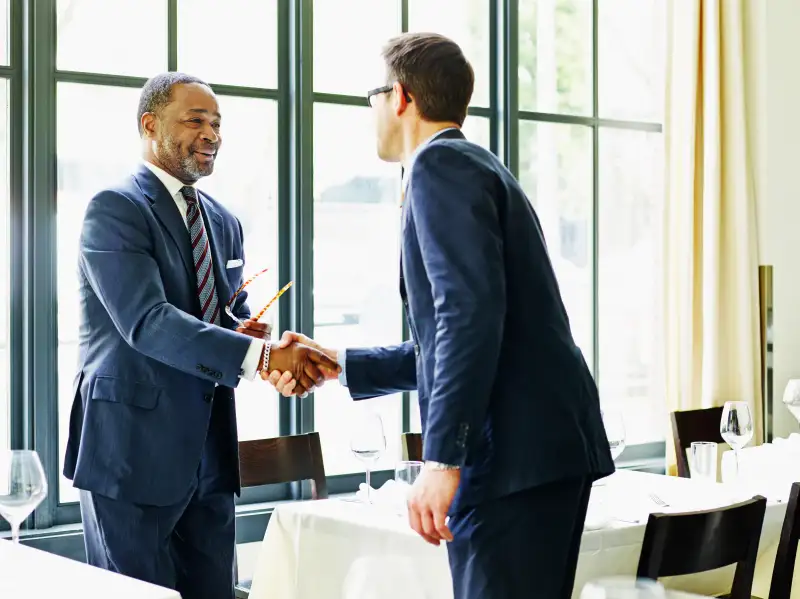 Two businessmen shaking hands at lunch meeting