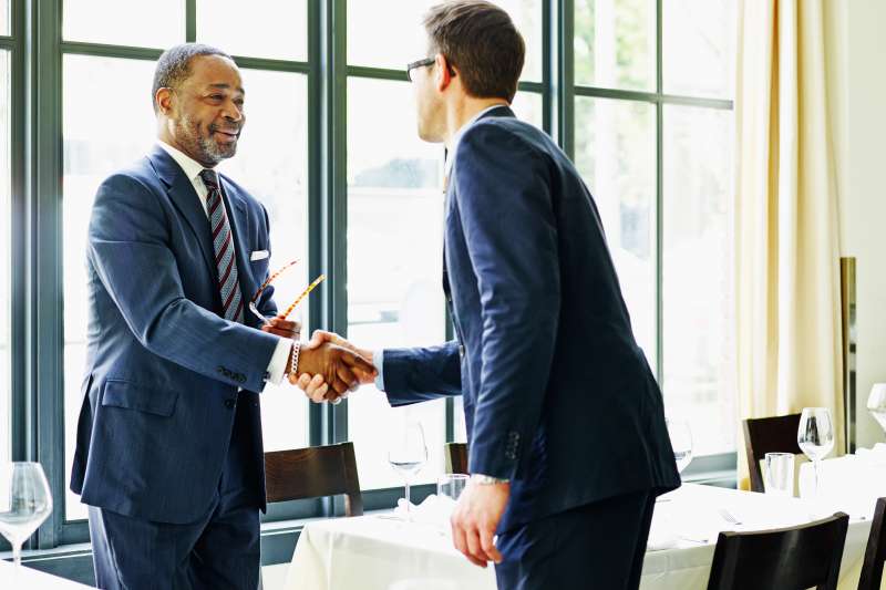 Two businessmen standing shaking hands at lunch meeting in restaurant