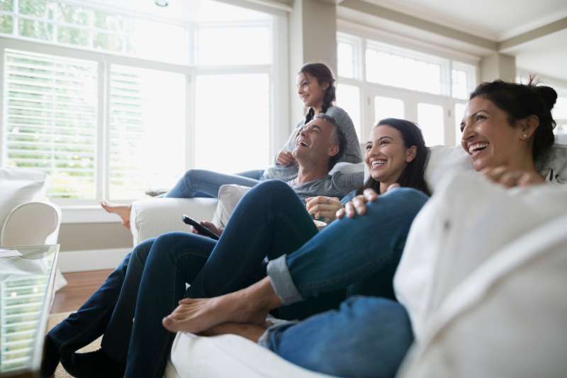 Family laughing watching TV on living room sofa