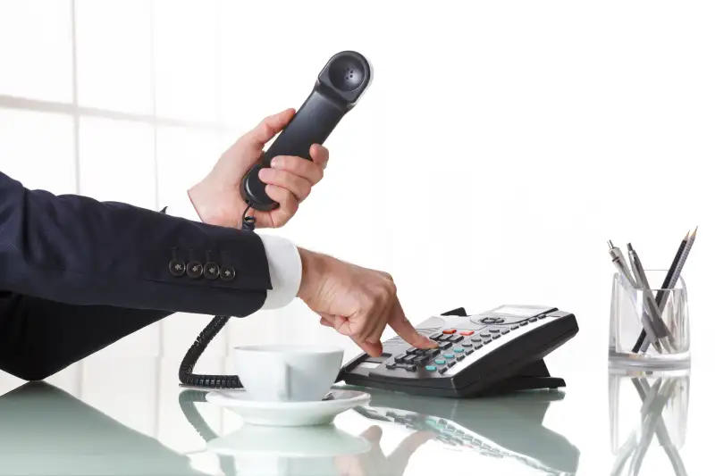 Businessman hands dialing out on a black deskphone