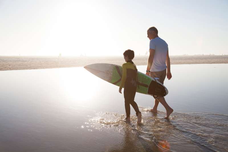 Man walking with grandson carrying surf board