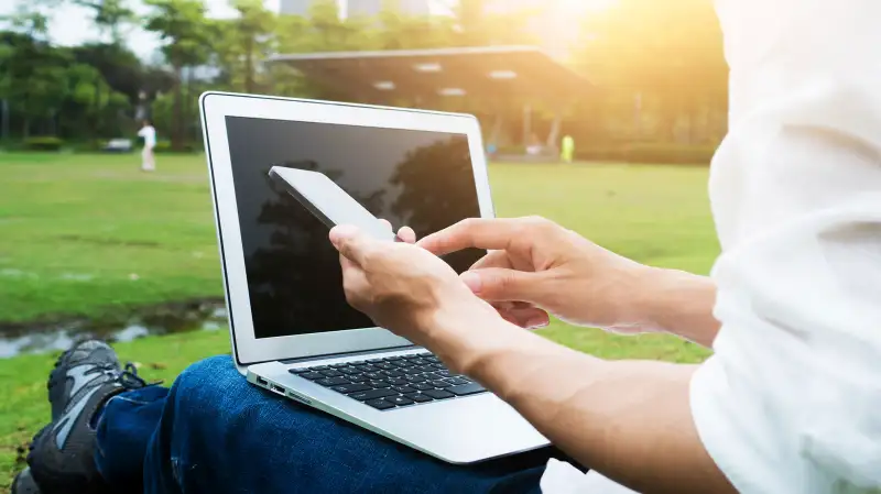 person laying on grass with laptop and cell phone