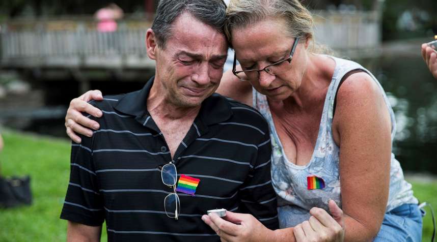 Two mourners with Gay flags pinned to their shirts grieve during a vigil for the victims of the terrorist massacre at the gay night club, Pulse, at Eola Lake in Orlando, USA on June 12, 2016.