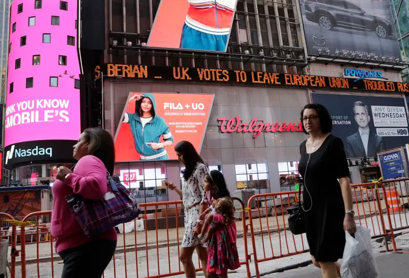 People walk past a news ticker that reads  U.K. Votes to Leave European Union,  Friday, June 24, 2016, in New York's Times Square. Britain voted to leave the European Union after a bitterly divisive referendum campaign, sending global markets plunging, casting British politics into disarray.