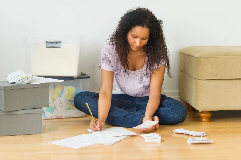 Hispanic woman sitting on floor paying bills