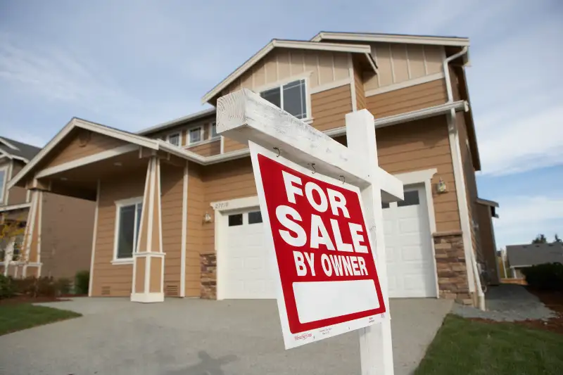 'For Sale' sign in front of house (focus on sign)