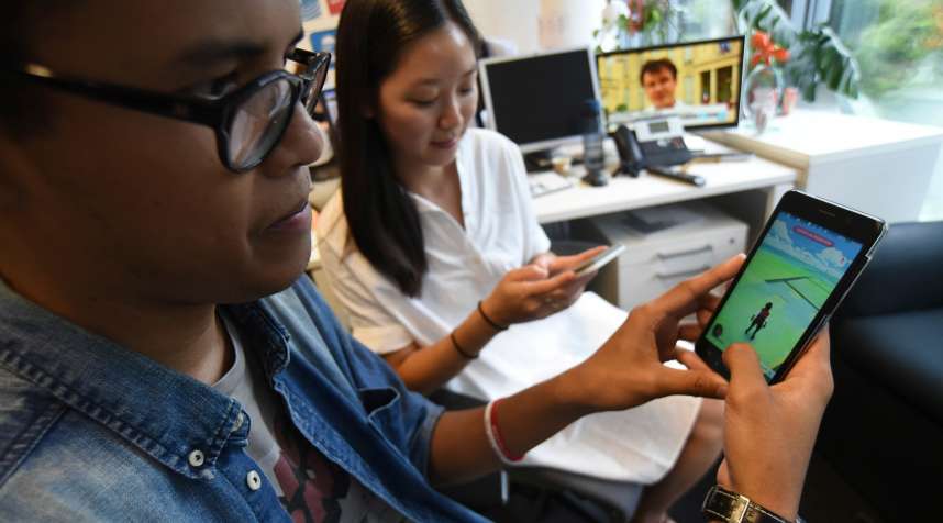 Youths play with the Pokemon Go app on their smartphone. Millions of users have already downloaded the game, which requires users to catch on-screen pokemon characters using their real-world location. Shares in the gaming company Nintendo jumped by nearly a quarter following the app success.