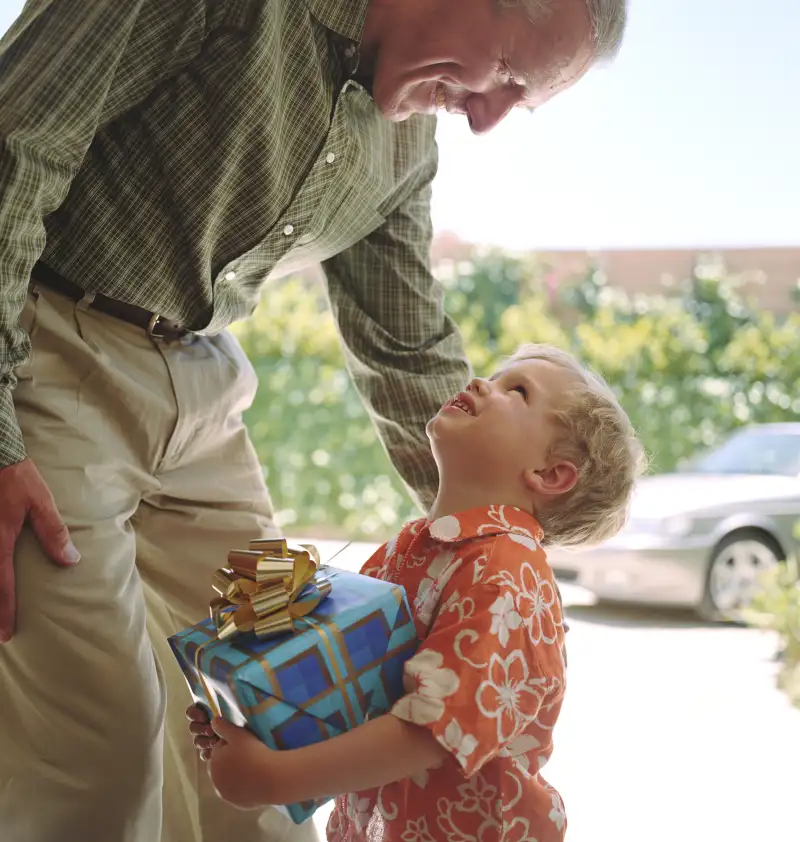Boy (2-4) holding present looking up at mature man, close-up