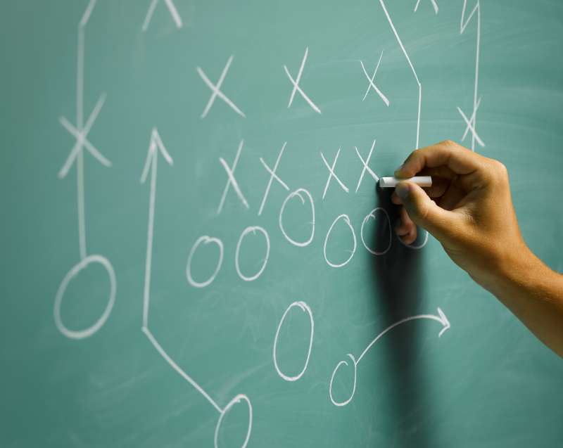 Man drawing football play diagram on blackboard, close-up