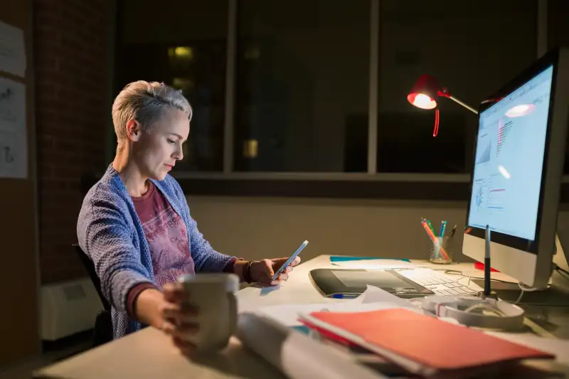 Designer with cell phone working late at desk