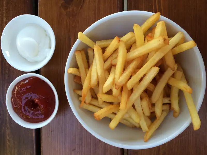 Directly Above Shot Of French Fries In Bowl By Sauce On Wooden Table