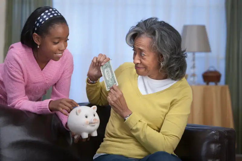 African woman giving granddaughter dollar bill for piggy bank