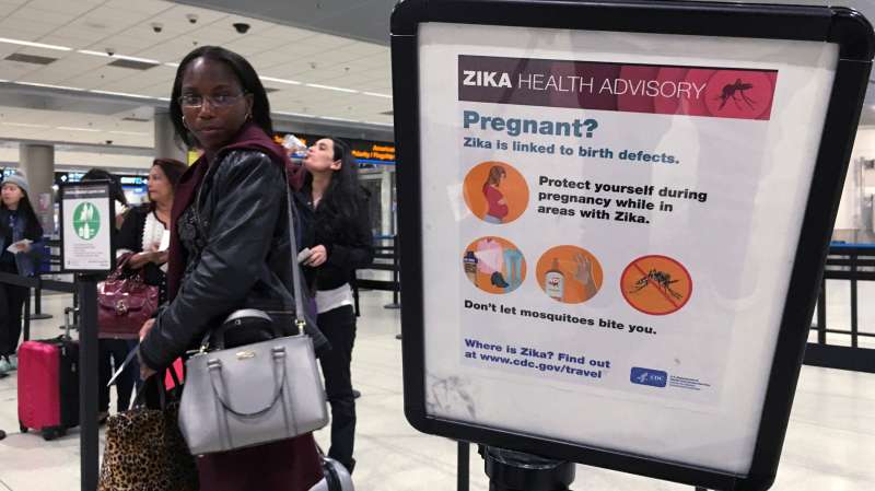A woman looks at a Center for Disease Control (CDC) health advisory sign about the dangers of the Zika virus as she lines up for a security screening at Miami International Airport in Miami, Florida, May 23, 2016.