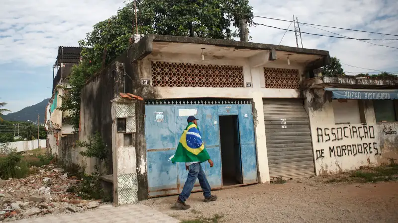 A resident walks while wearing a Brazilian flag in the mostly demolished Vila Autodromo favela community on February 24, 2016 in Rio de Janeiro, Brazil. Most residents of the favela community have moved out and had their properties demolished after receiving compensation for their homes which are located directly adjacent to the Olympic Park under construction for the Rio 2016 Olympic Games. A small fraction of remaining families from an original 700 or so in Vila Autodromo are resisting the controversial evictions and remain in the community. The favela sprang from an old fishing community and was considered one of the city's safest. Removals and demolitions have occurred in other Rio communities with tangential links to the games.