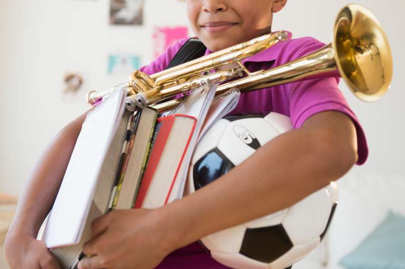 child carrying soccer ball and trumpet and books