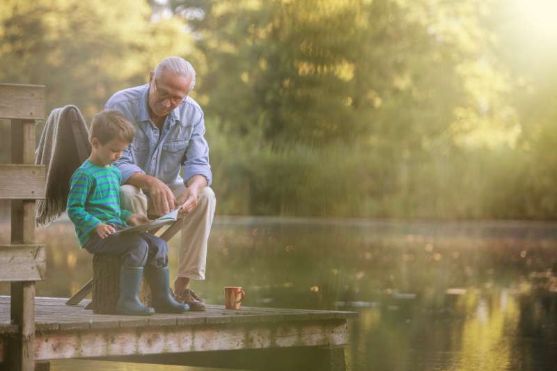 Grandfather and grandson reading at lake