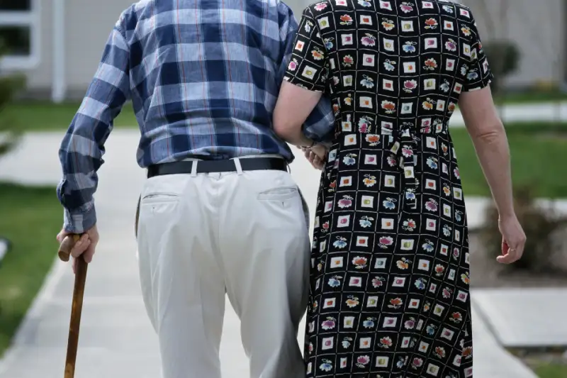 man walking with cane, being helped by woman