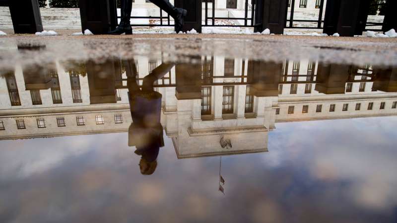A woman walks past the Marriner S. Eccles Federal Reserve building as it is reflected in a puddle of water in Washington, D.C., on Jan. 27, 2015.
