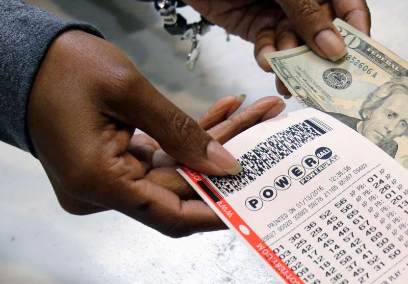 In this Jan. 13, 2016 file photo, a clerk hands over a Powerball ticket for cash at Tower City Lottery Stop in Cleveland.
