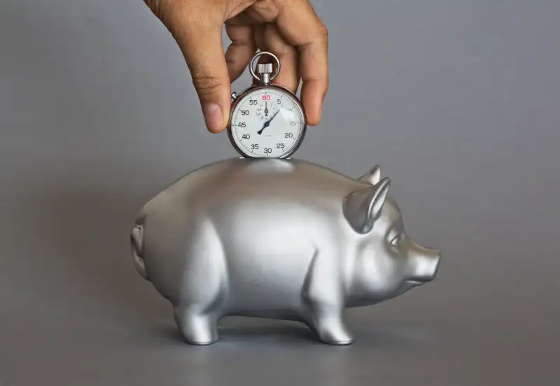 Hand putting stopwatch into silver piggy bank