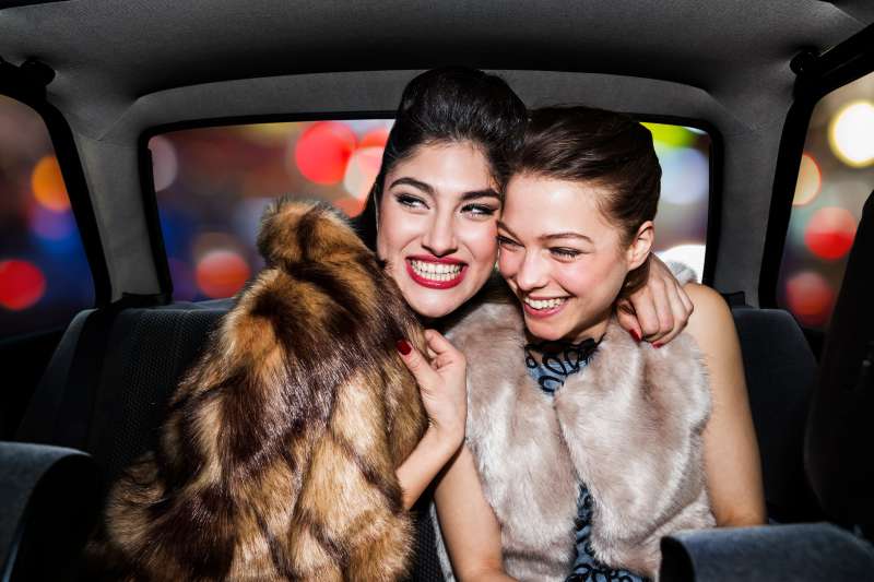 Women laughing in back of car, going out at night.