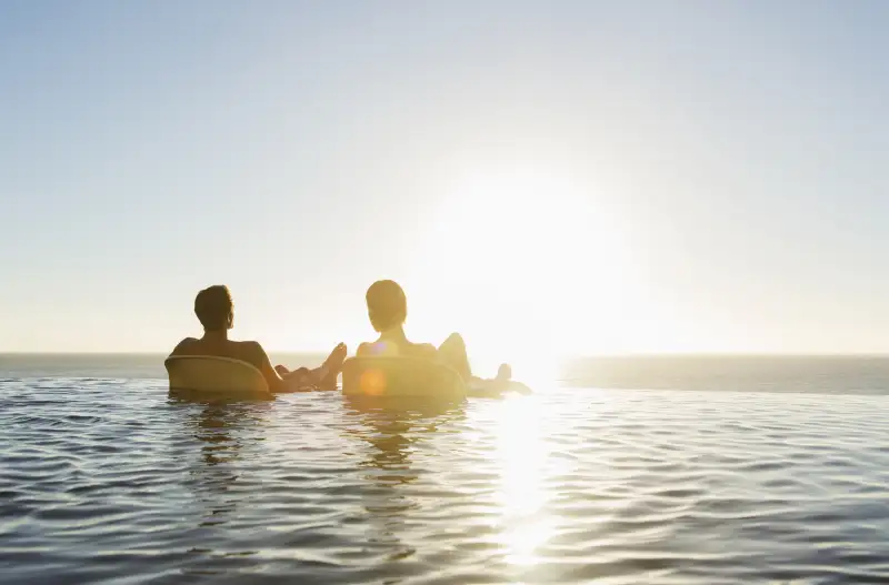 Couple in lounge chairs in infinity pool overlooking ocean