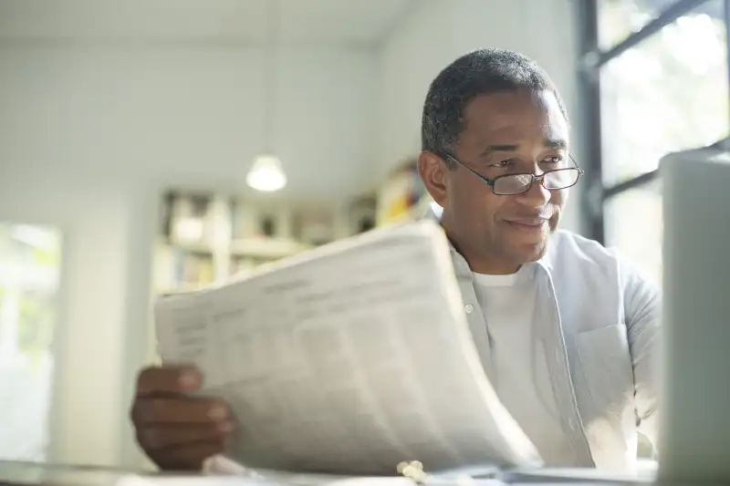 Senior man with newspaper using laptop