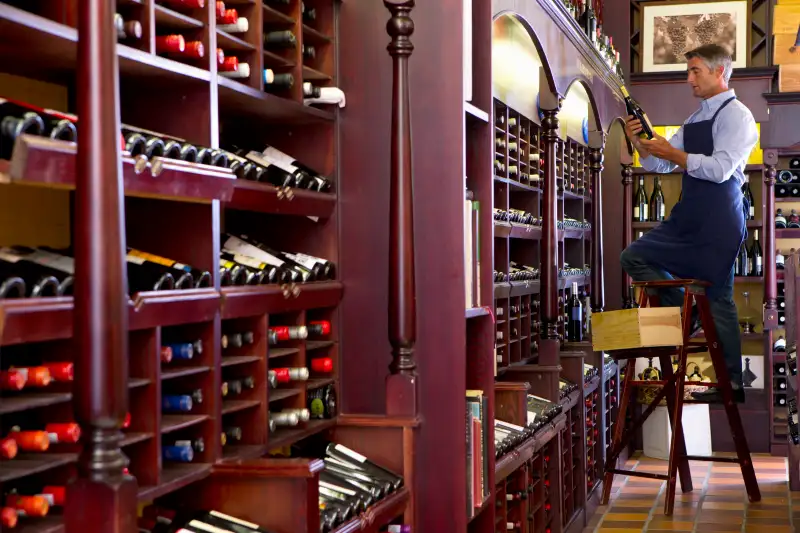 Worker on ladder stocking bottles in wine shop