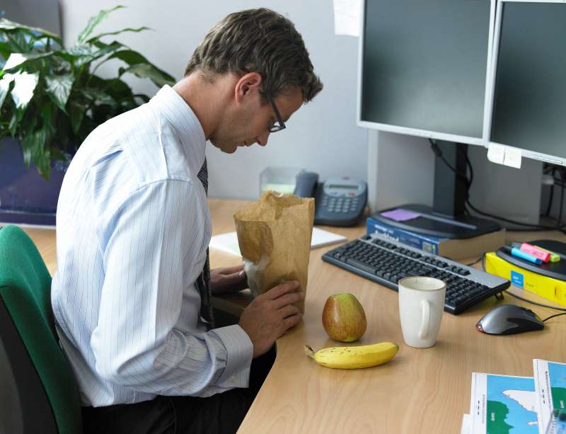 Business man at desk peering into lunch bag