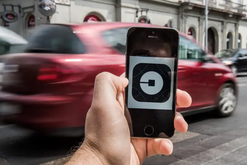 A customer holds an Apple Inc. iPhone displaying the Uber Technologies Inc. car service taxi application (app) logo as a vehicle passes by in this arranged photograph in Budapest, Hungary, on Wednesday, July 13, 2016.