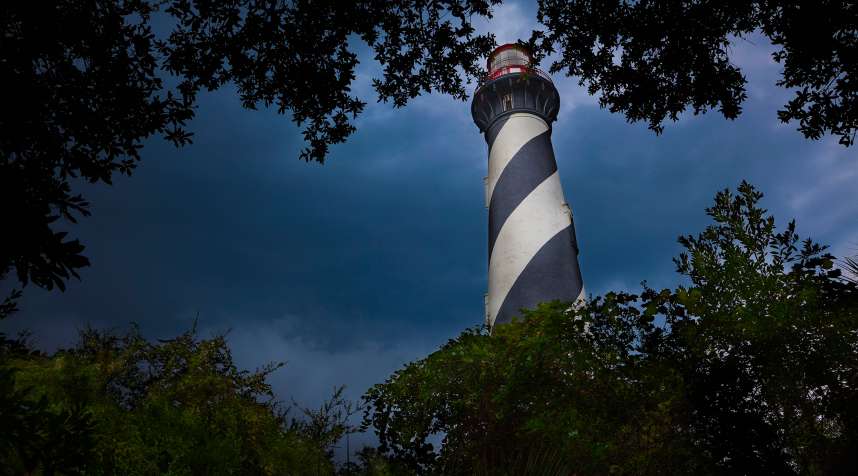 Lighthouse viewed through the trees and vegetation with dark and moody clouds in the sky; St. Augustine, Florida