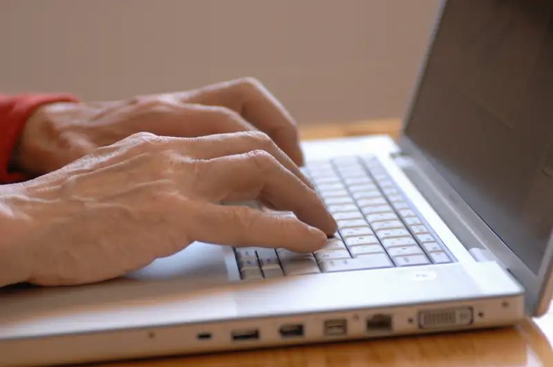 Senior man using laptop, side view, close-up of hands