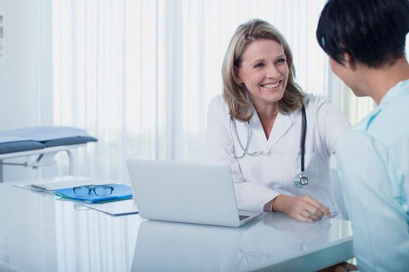 Smiling female doctor and woman sitting at desk in office