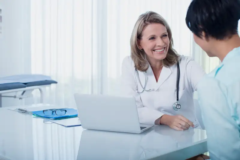 Smiling female doctor and woman sitting at desk in office