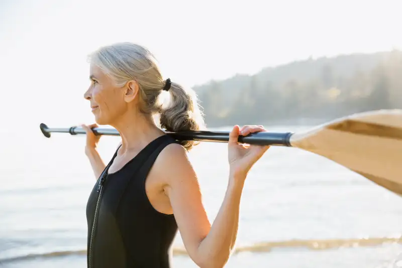 Senior woman holding paddle on sunny beach