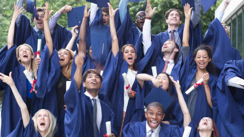 Group portrait of students in graduation gowns throwing mortarboards in the air
