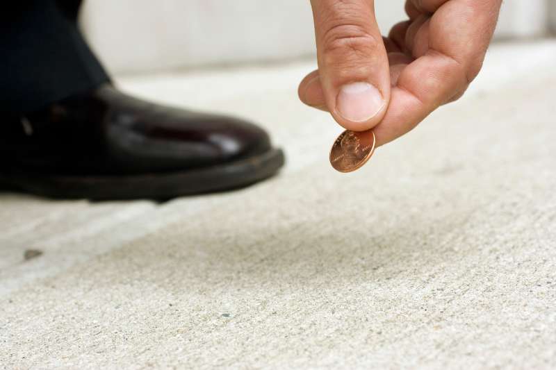 Close up of man picking up penny from street