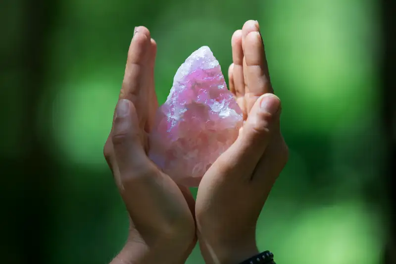 Hands holding healing crystal on green.