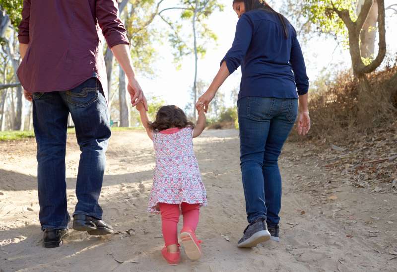 Parents and young daughter walk hand in hand on a rural path