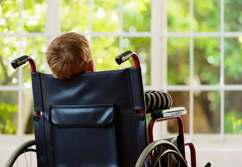 Backview of wheelchair-bound boy watching garden he cannot play in