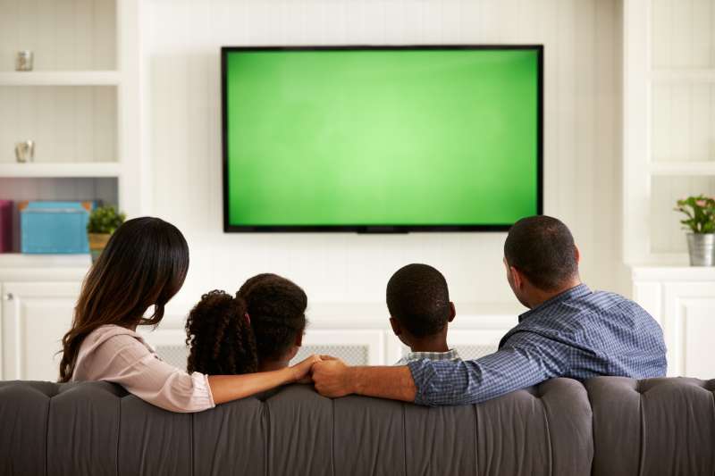 Parents and their two children watching TV together at home