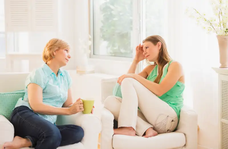 Mother and adult daughter sitting on sofa and talking