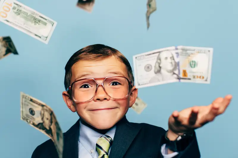 young boy in suit and glasses surrounded by falling money