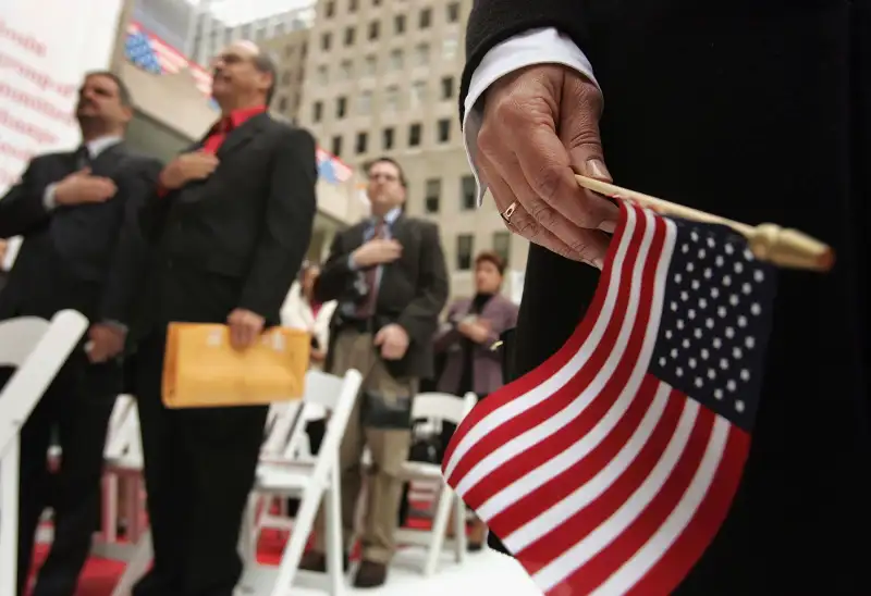 NEW YORK - OCTOBER 26: Attendees stand for the Pledge of Allegiance during a swearing-in ceremony for new U.S. citizens October 26, 2004 in New York City. In recognition of  Democracy Plaza  at Rockefeller Center, Alfonso Aguilar, chief of the Office of Citizenship for U.S. Citizenship and Immigration Services (USCIS), administered the Oath of Allegiance to 25 new Americans from 21 different countries.