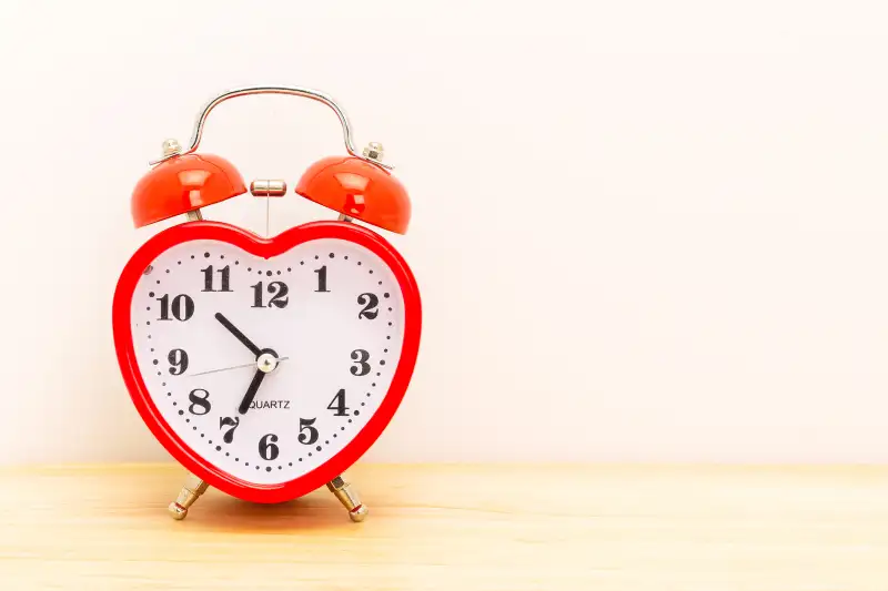 Heart shaped alarm clock on a wooden surface against a white background