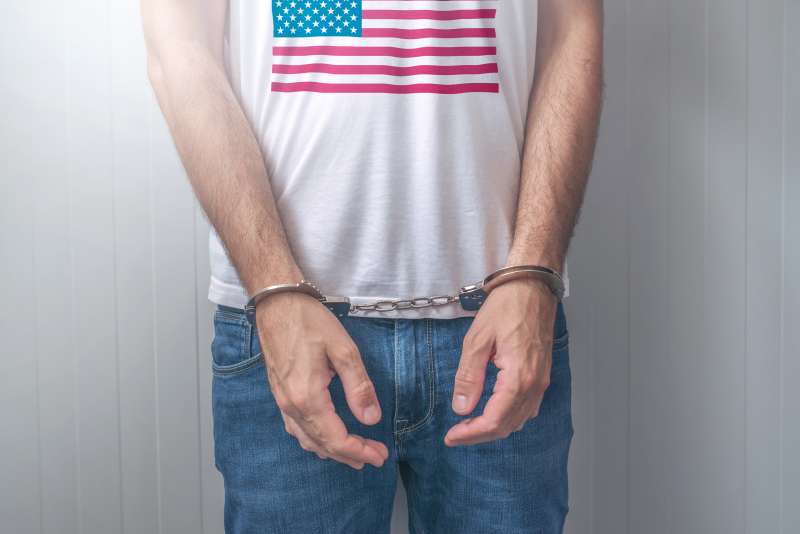 Arrested man with cuffed hands wearing shirt with USA flag