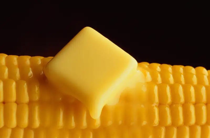 Knob of butter melting over corn on the cob, black background